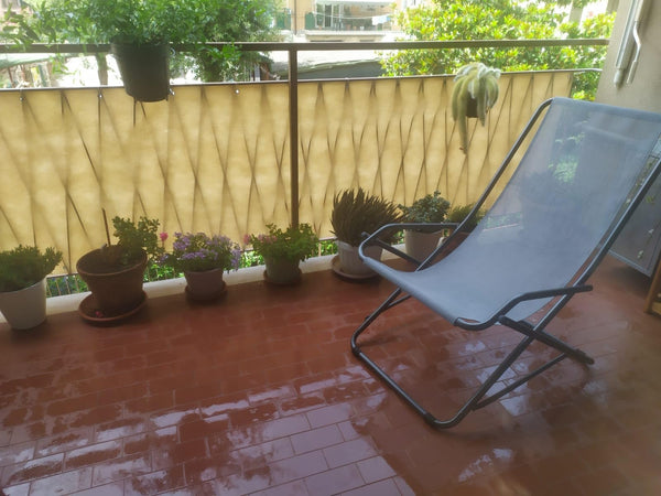 Balkon z beżową osłoną na balustradzie, roślinami w doniczkach na posadzce i leżakiem